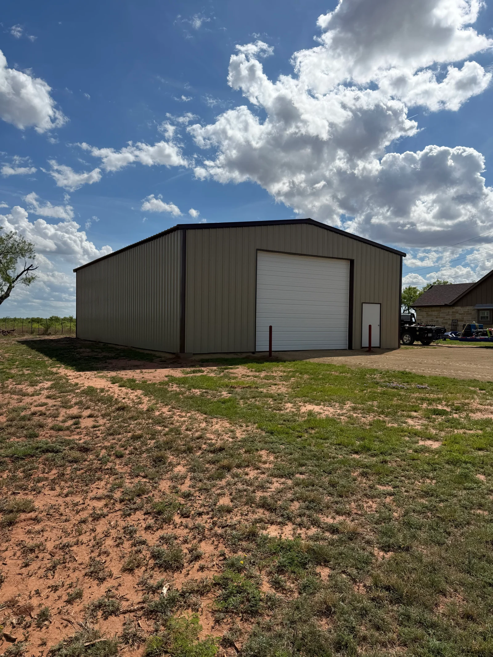 Corrugated metal storage building with white overhead door and side entry on gravel lot